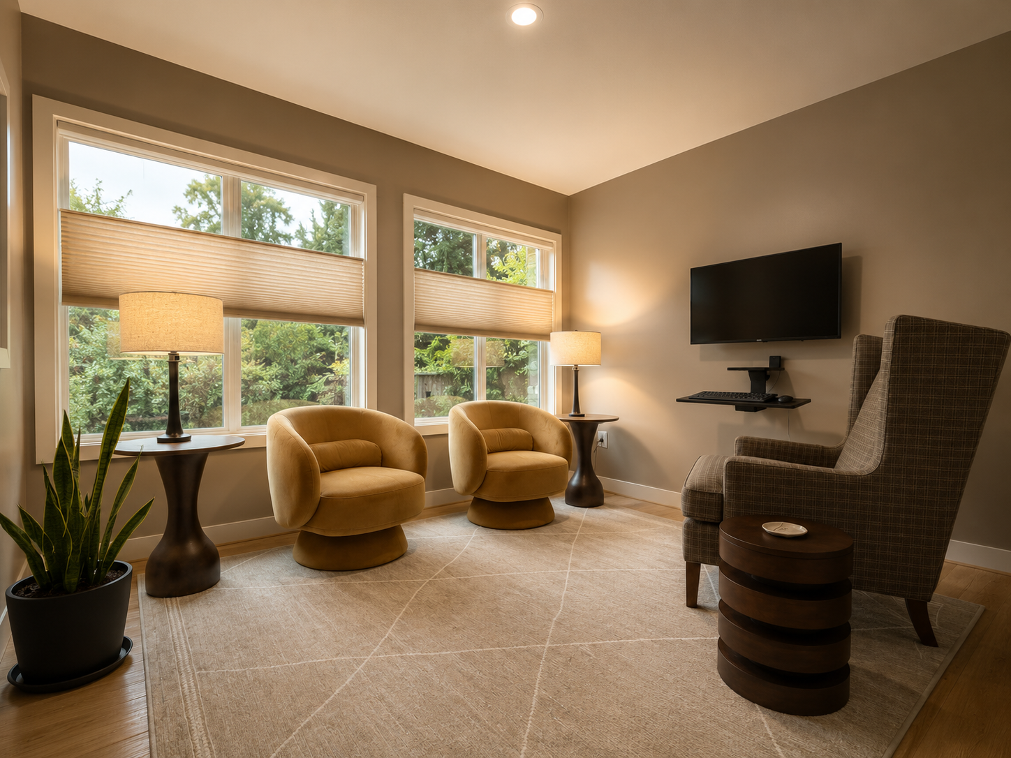 Bainbridge Direct Primary Care consultation room — warm taupe walls, two golden ochre swivel chairs, large windows to Pacific Northwest trees, wing chair, table lamps, integrated display