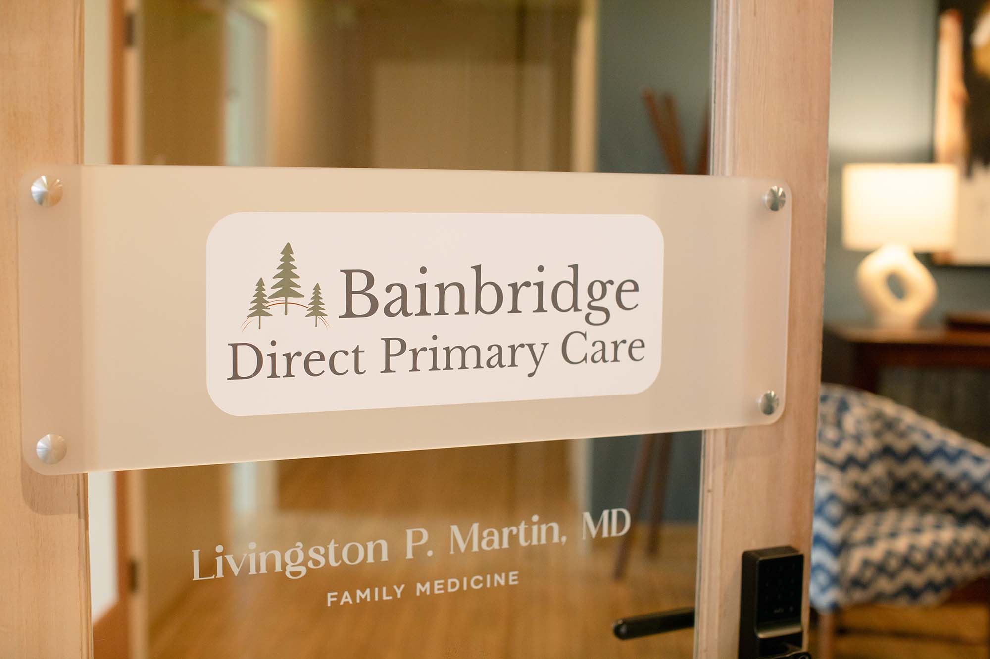 Bainbridge Direct Primary Care restroom — deep slate blue walls, brass grab bars integrated as design element, botanical watercolor art, warm lighting