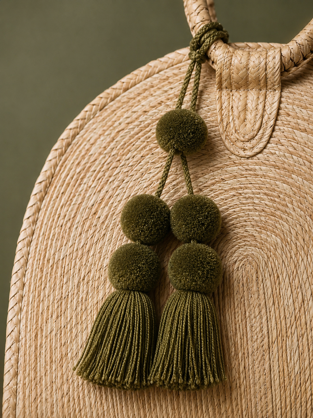 Beck Road lifestyle detail — woven straw bag with olive green pom-pom tassels against sage backdrop