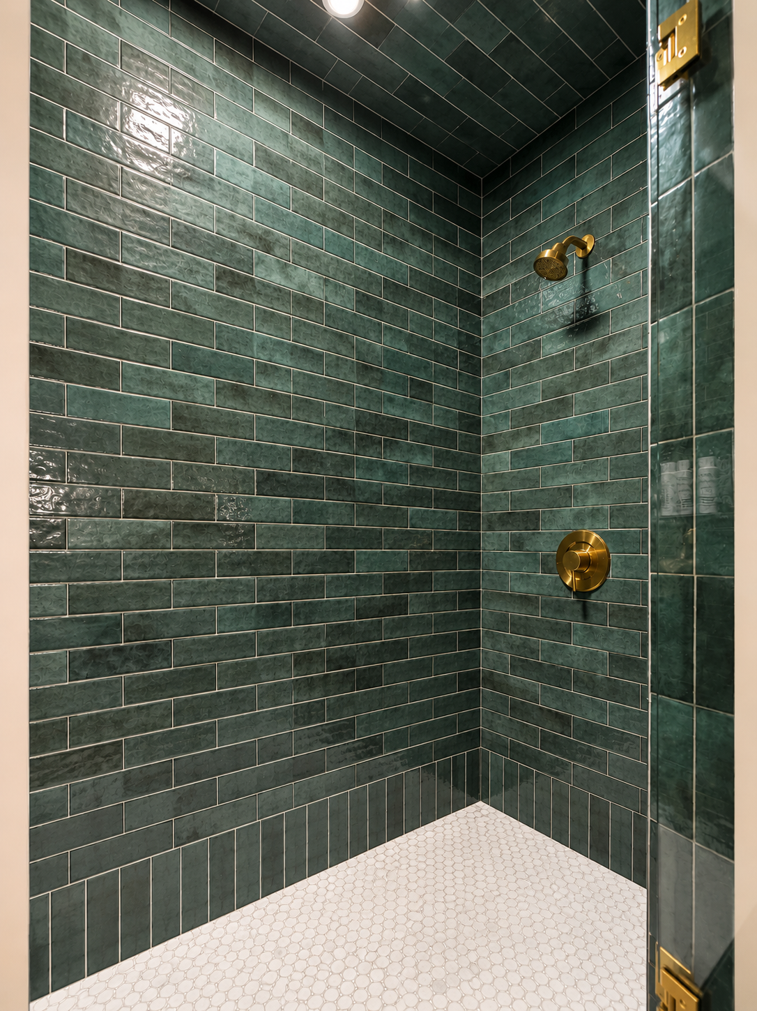 Beck Road guest shower — floor-to-ceiling deep green glazed tile, white hex penny tile floor, brass fixtures and hardware