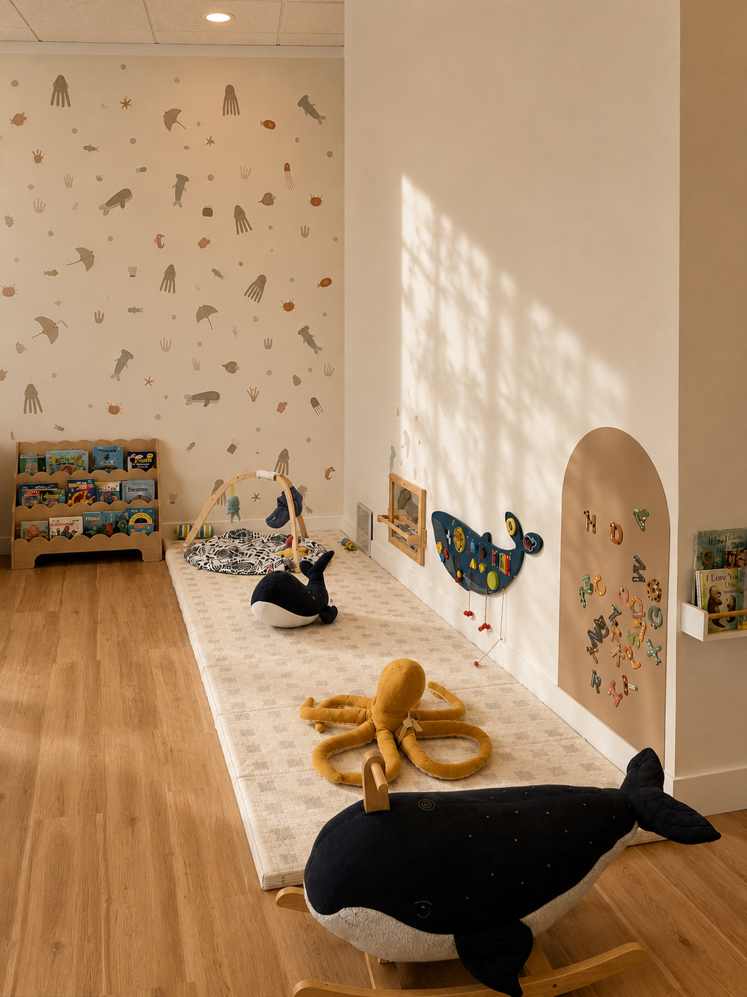 Bainbridge Play Cafe infant zone — padded play mat, ocean-theme wallpaper, arched alcove with letter magnets, whale plush toys