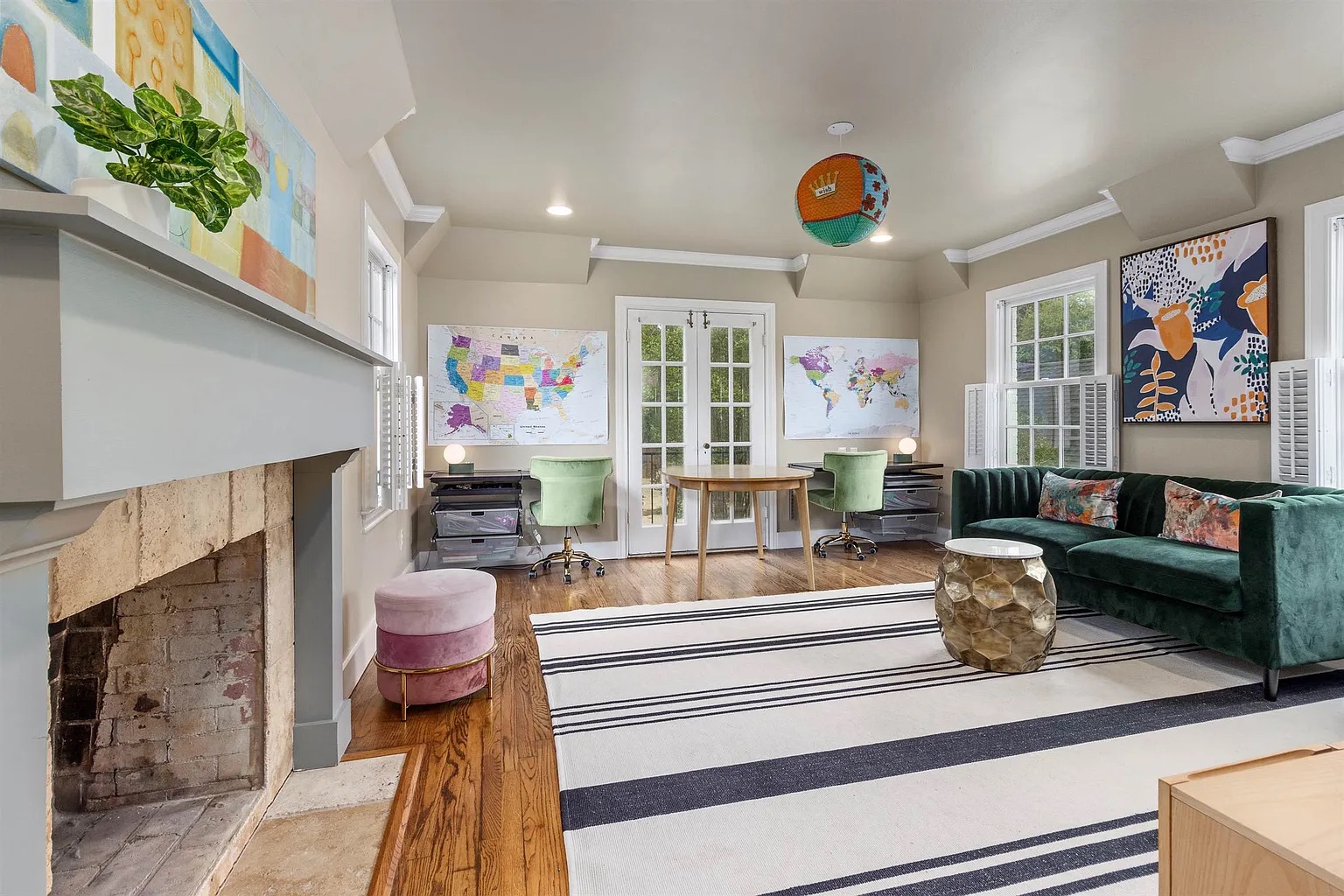 Tyler Estate children's study — colourful art, green velvet chairs, dark emerald sofa, striped rug, globe pendant, world maps, brick fireplace
