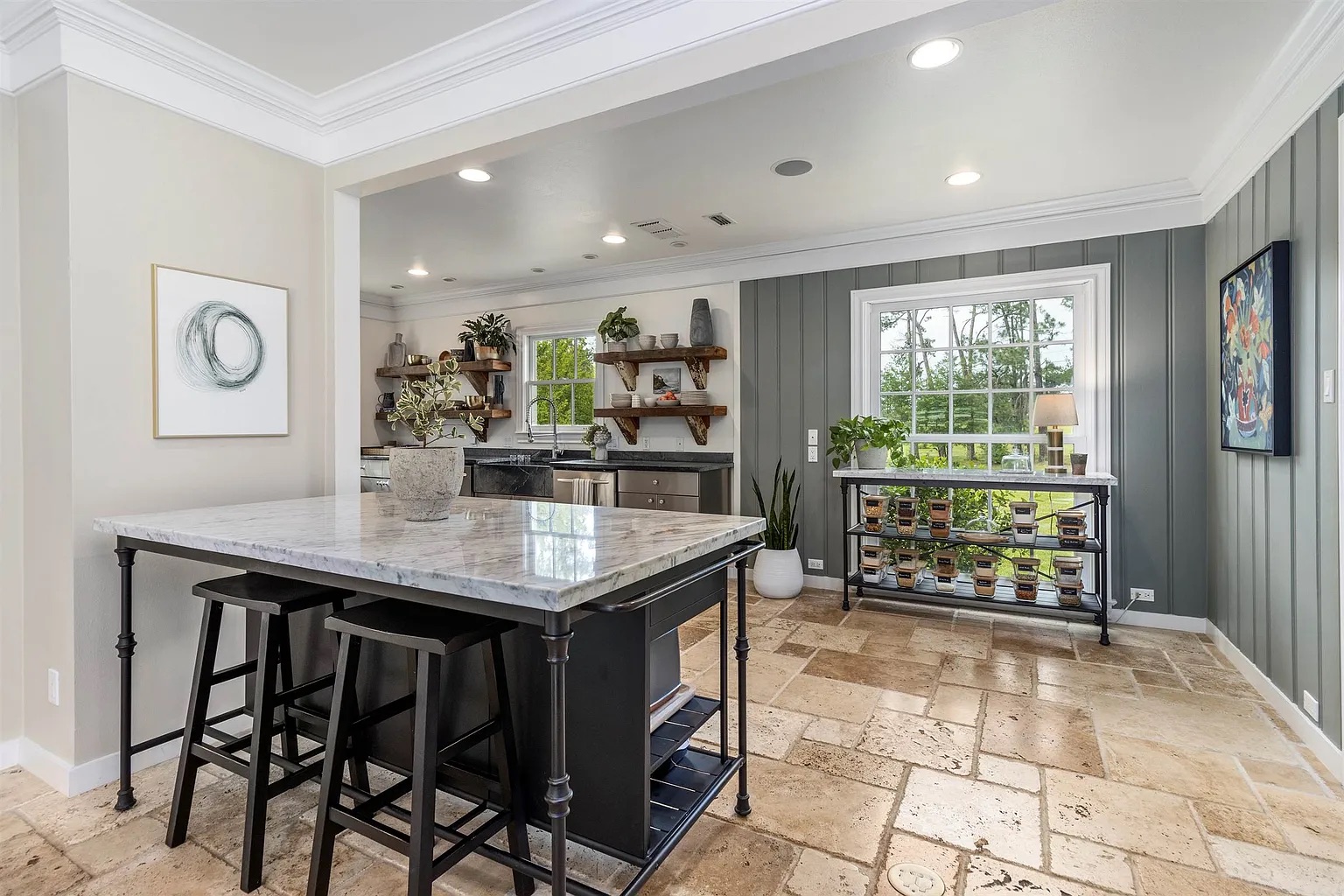 Tyler Estate kitchen — marble island with black iron stools, green board-and-batten accent wall, open oak shelving, stone tile floor