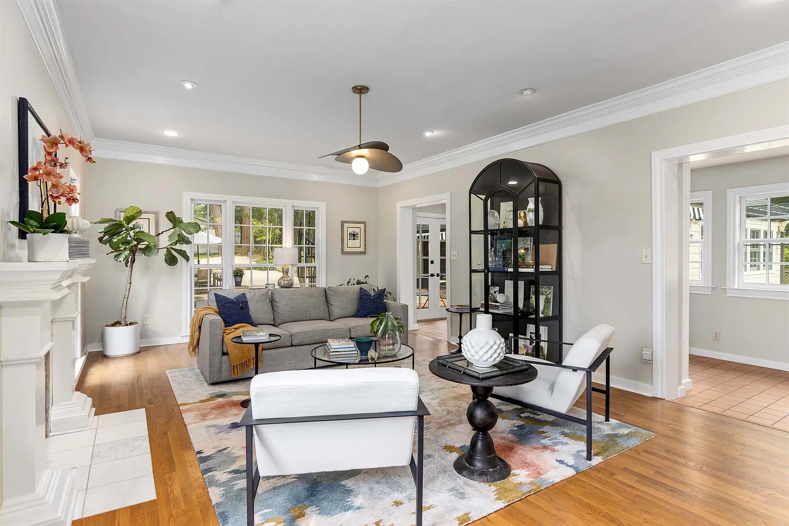 Tyler Estate living room — grey sofa, arched black display cabinet, modern ceiling fan, white fireplace mantel, colourful abstract rug