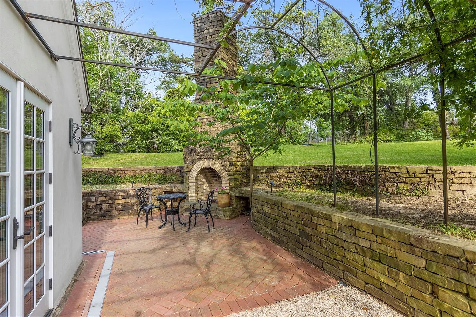 Tyler Estate outdoor fireplace — brick arched fireplace with iron trellis pergola, stone retaining walls, brick patio, East Texas garden view