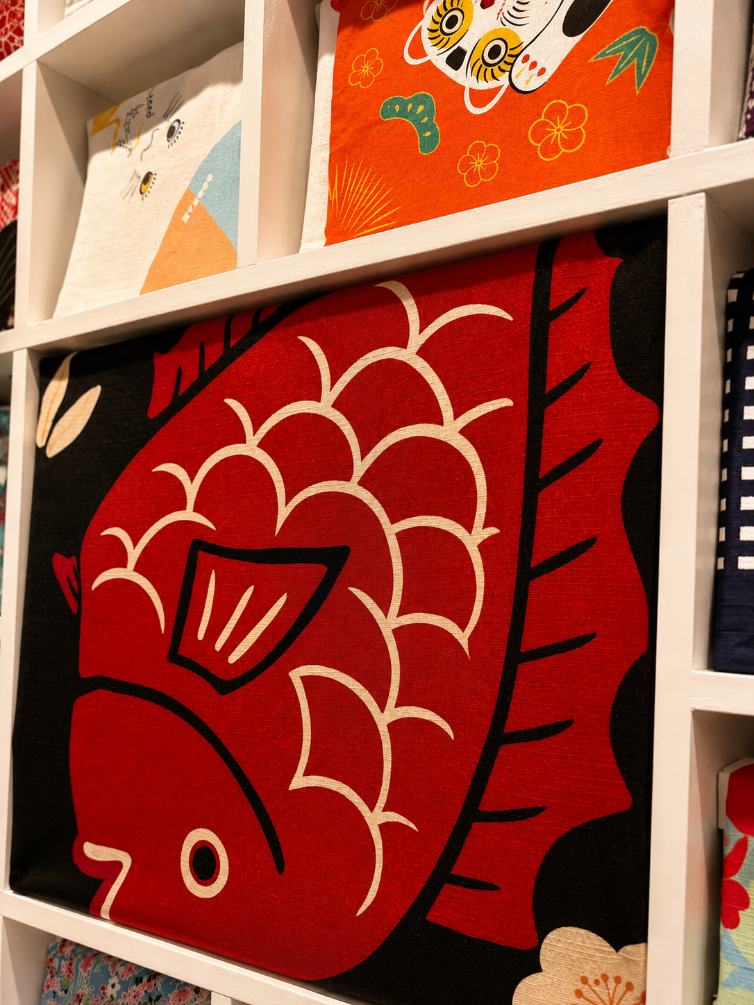 Lunamira furoshiki detail — bold red koi fish Japanese wrapping cloth in white display cubby, graphic and vibrant